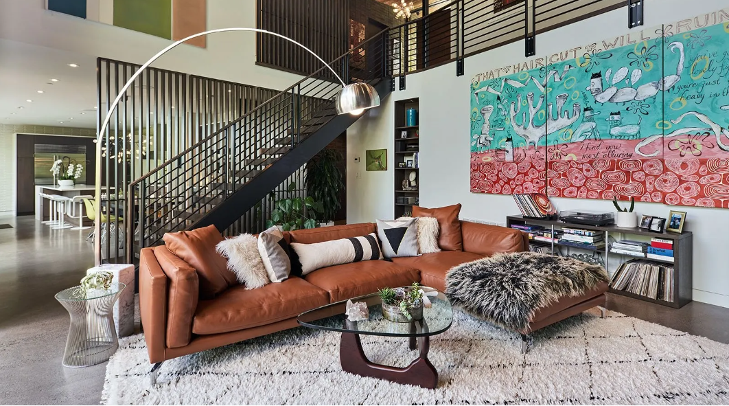 Modern living room with a brown sectional sofa, glass coffee table, and colorful wall art.